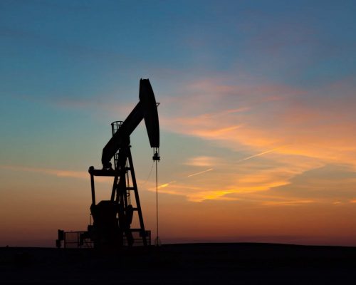 A single oil well pumpjack silhouetted against a prairie sunset